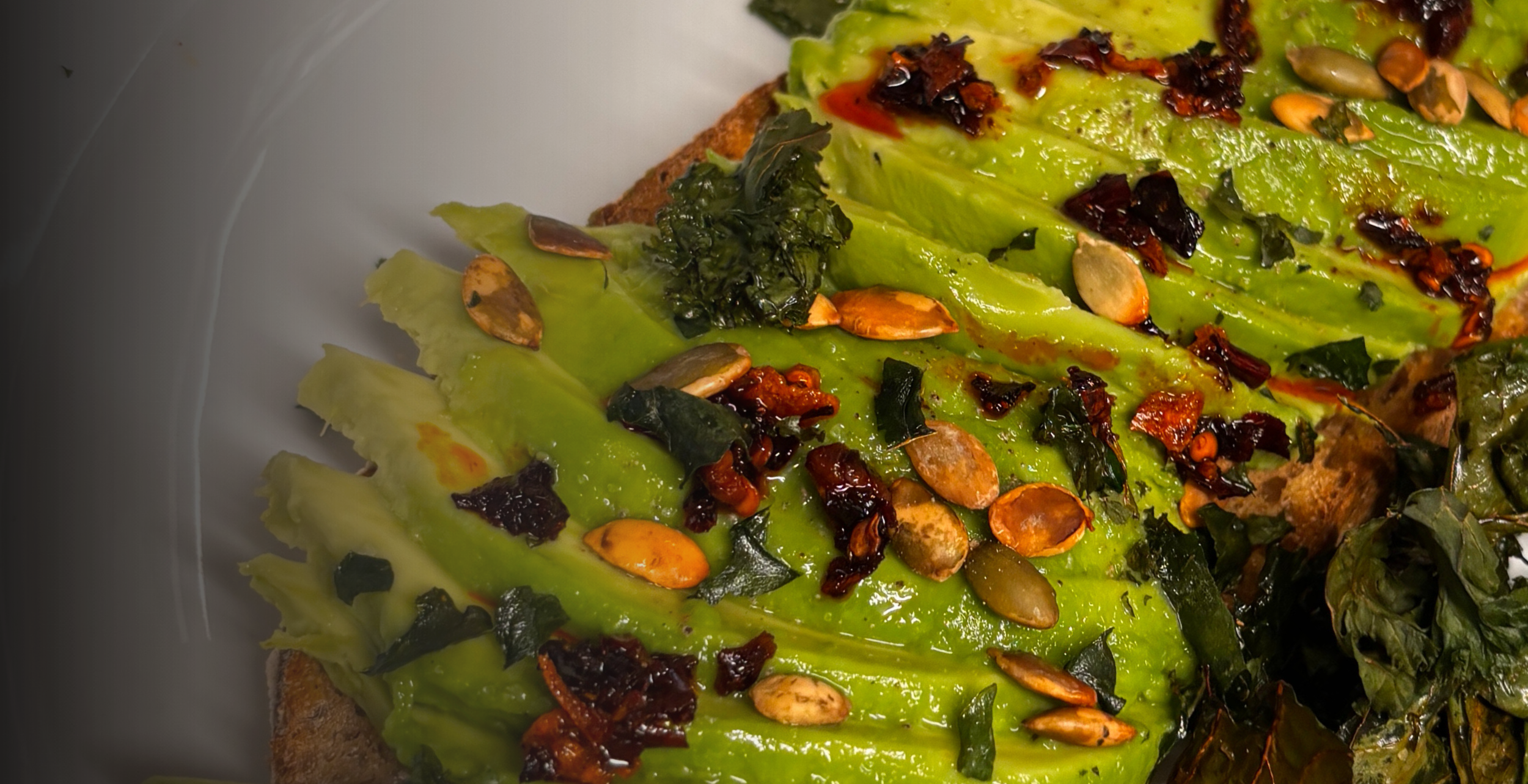 Sourdough Toast topped with sliced avocado, chilli crisp, pumpkin seeds and crispy kale
